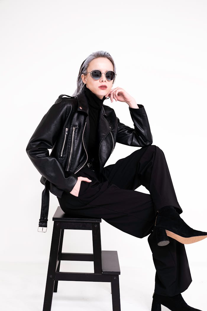 Fashionable woman in a black leather jacket posing in a minimalist studio setting.